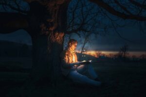 man sitting under a tree reading glowing book at night